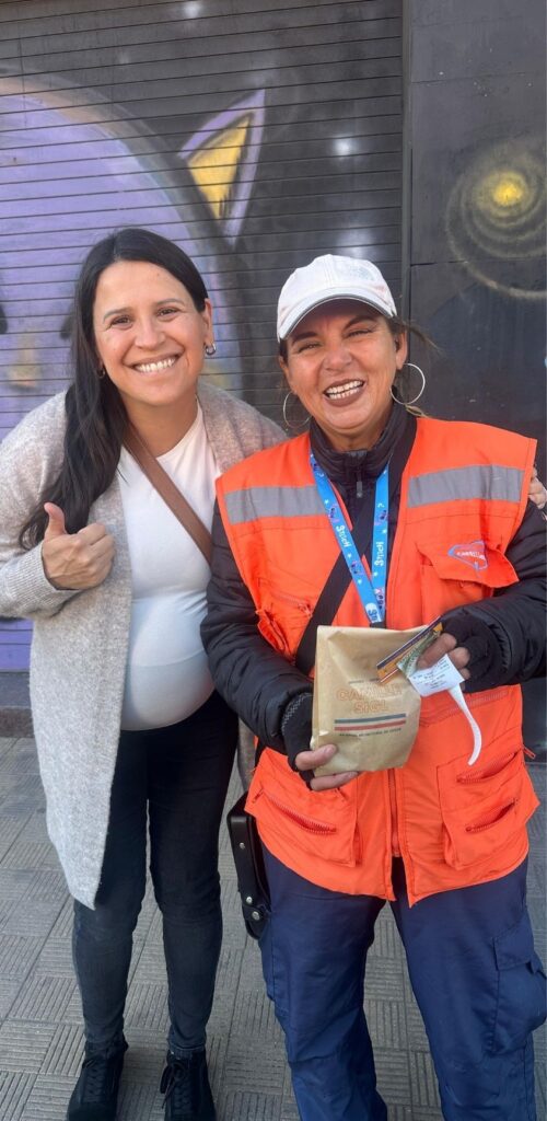 Camille sigl, sonriendo junto a una mujer trabajadora del distrito 12 también sonriendo, ambas felices. Foto de la galería Camille Sigl en la feria de La Florida.